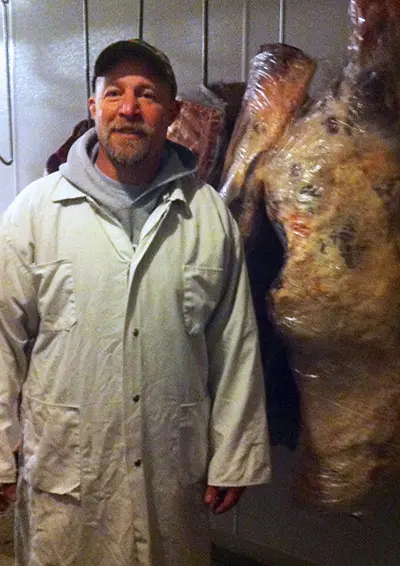 Ted Baker standing next to meat hanging on a scale